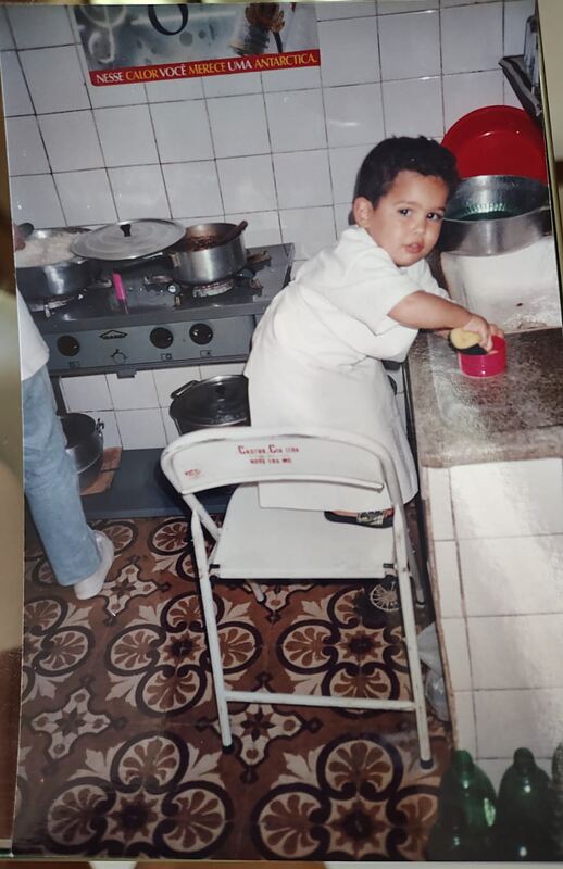 Daniel ainda pequeno, em pé numa cadeira, cortando massa na cozinha do bairro Amazonas